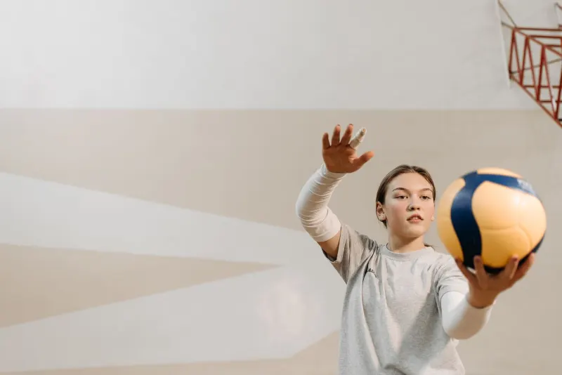 Aydınlık bir spor salonunda servis atmaya hazırlanan genç voleybolcu